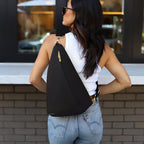 Woman wearing the black Canvelle Contour Sling Bag across the back to show hands-free crossbody fit and gold hardware.