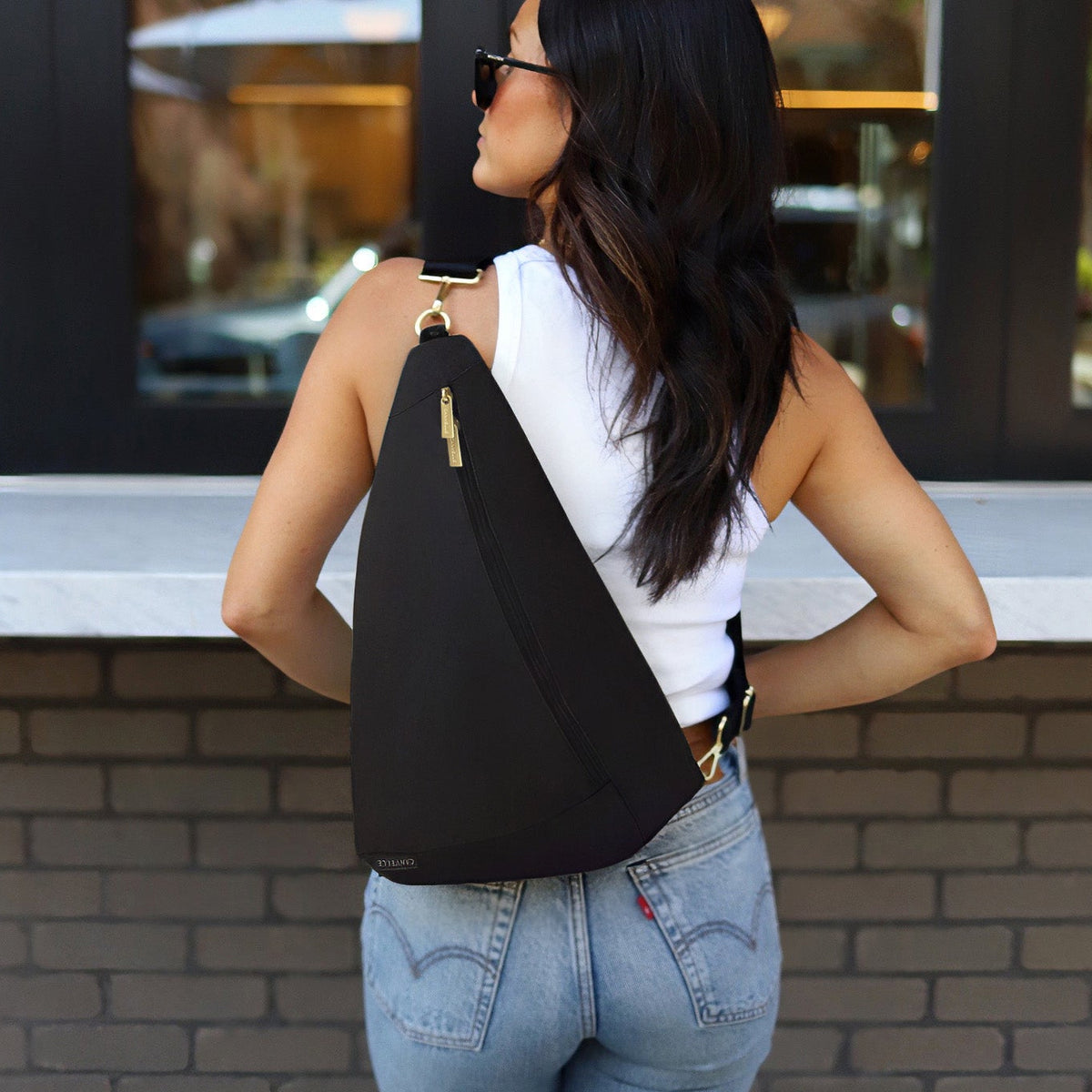 Woman wearing the black Canvelle Contour Sling Bag across the back to show hands-free crossbody fit and gold hardware.