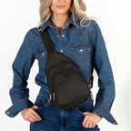 Woman wearing medium Canvelle City Sling Bag in black canvas across the chest over a denim shirt to demonstrate everyday size and hands-free fit.