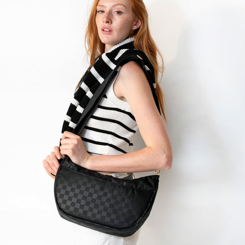 Medium black checkered Canvelle Crescent Bag worn at the hip with a striped top.