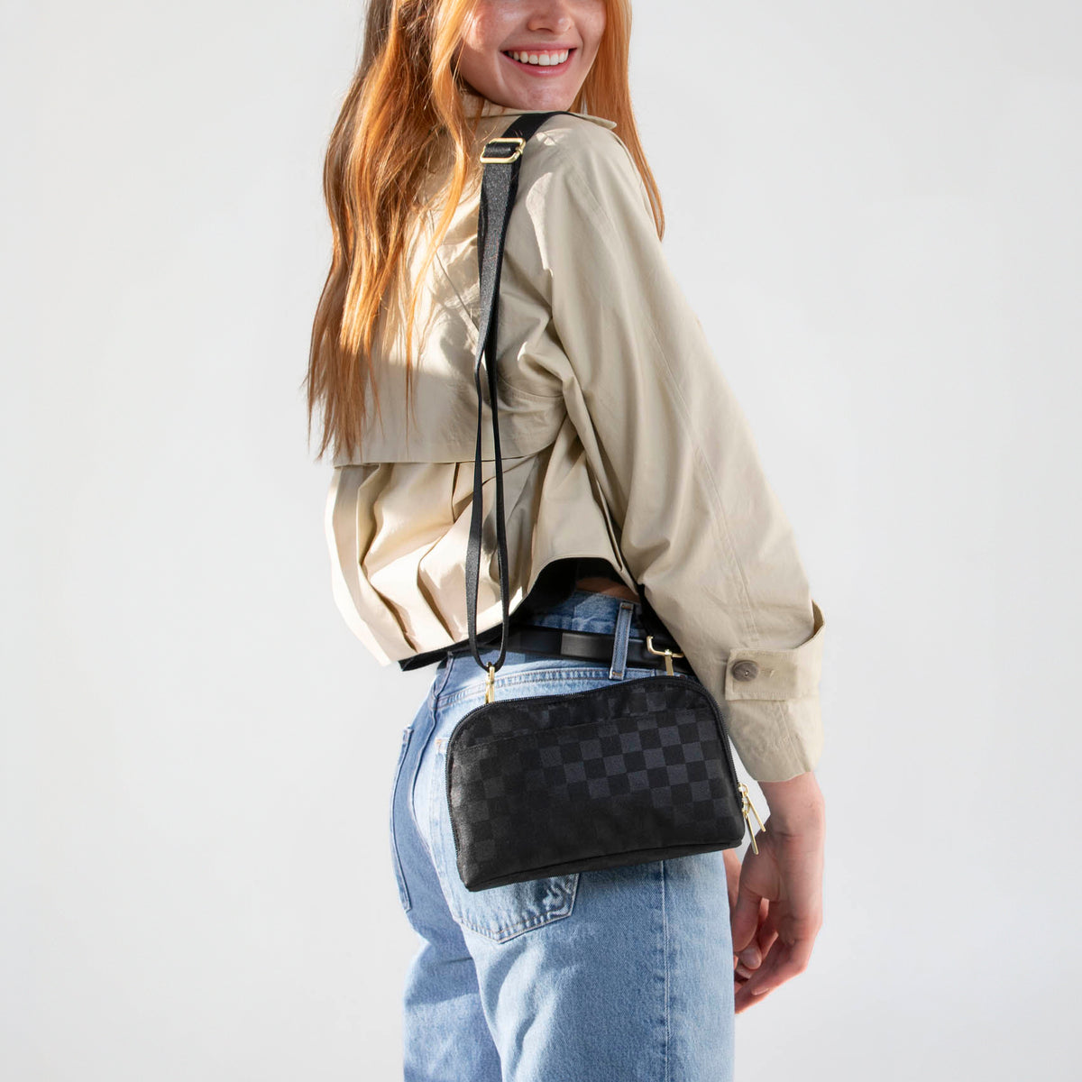 Woman wearing the Black Checkered Canvelle Crossbody Wallet crossbody with jeans and a trench coat