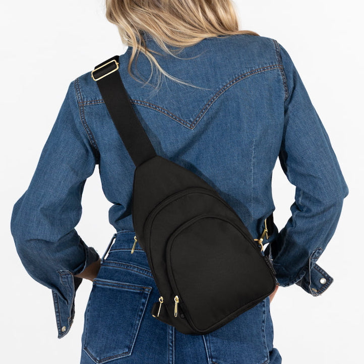 Woman wearing medium Canvelle City Sling Bag in black canvas across the back over a denim shirt to demonstrate everyday size and hands-free fit.