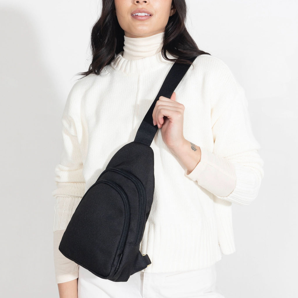 Woman wearing small Canvelle City Sling Bag in black canvas across the chest over a white sweater to demonstrate hands-free fit and size.