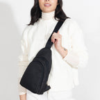 Woman wearing small Canvelle City Sling Bag in black canvas across the chest over a white sweater to demonstrate hands-free fit and size.