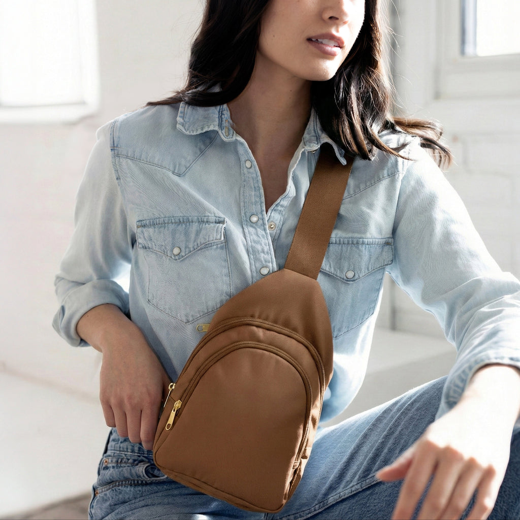 Woman wearing small Canvelle City Sling Bag in brown canvas across the chest over a denim shirt to demonstrate hands-free fit and casual style.