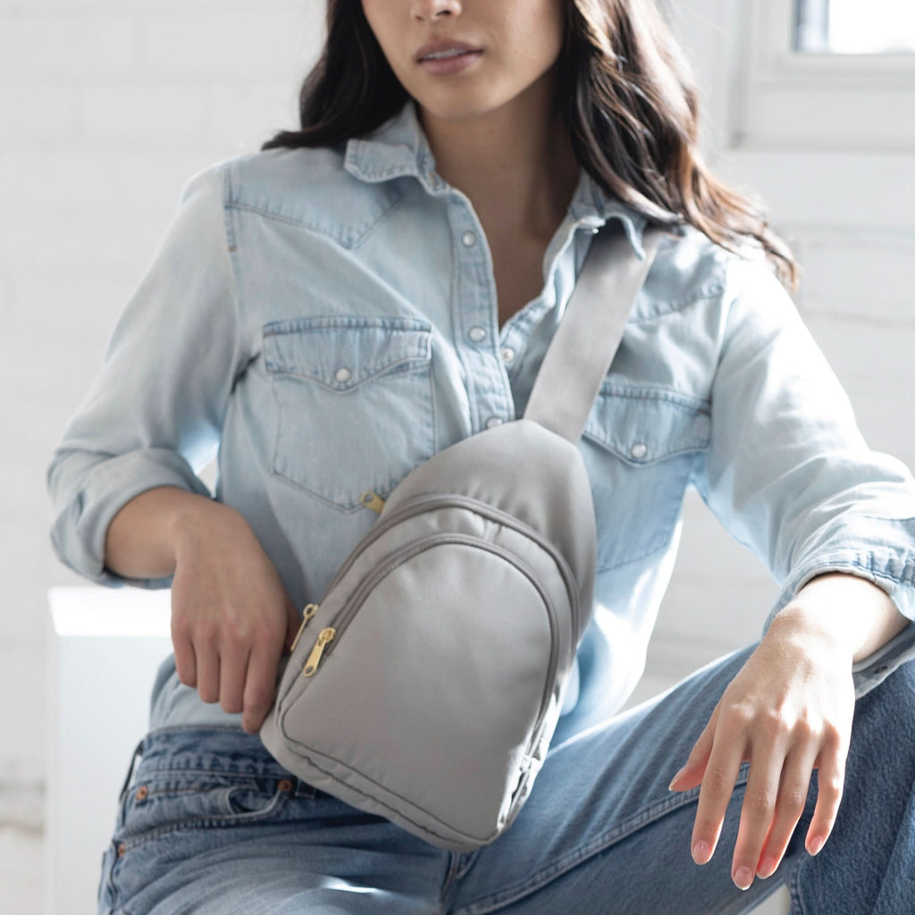Woman wearing small Canvelle City Sling Bag in grey canvas across the chest over a denim shirt to demonstrate hands-free casual style.