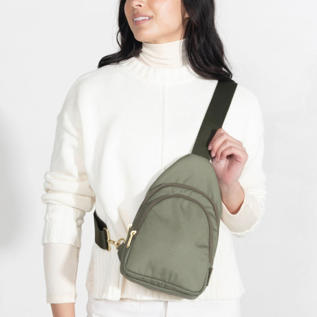 Woman wearing small Canvelle City Sling Bag in olive green canvas across the chest over a cream sweater to demonstrate hands-free fit and size.