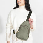 Woman wearing small Canvelle City Sling Bag in olive green canvas across the chest over a cream sweater to demonstrate hands-free fit and size.