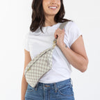 A woman modeling a white t-shirt, blue jeans, and brown boots, carrying a beige and white checkered shoulder bag against a plain white background.