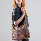 Woman wearing the large brown leopard Canvelle Hobo Handbag crossbody from a side angle to show the fit and profile.