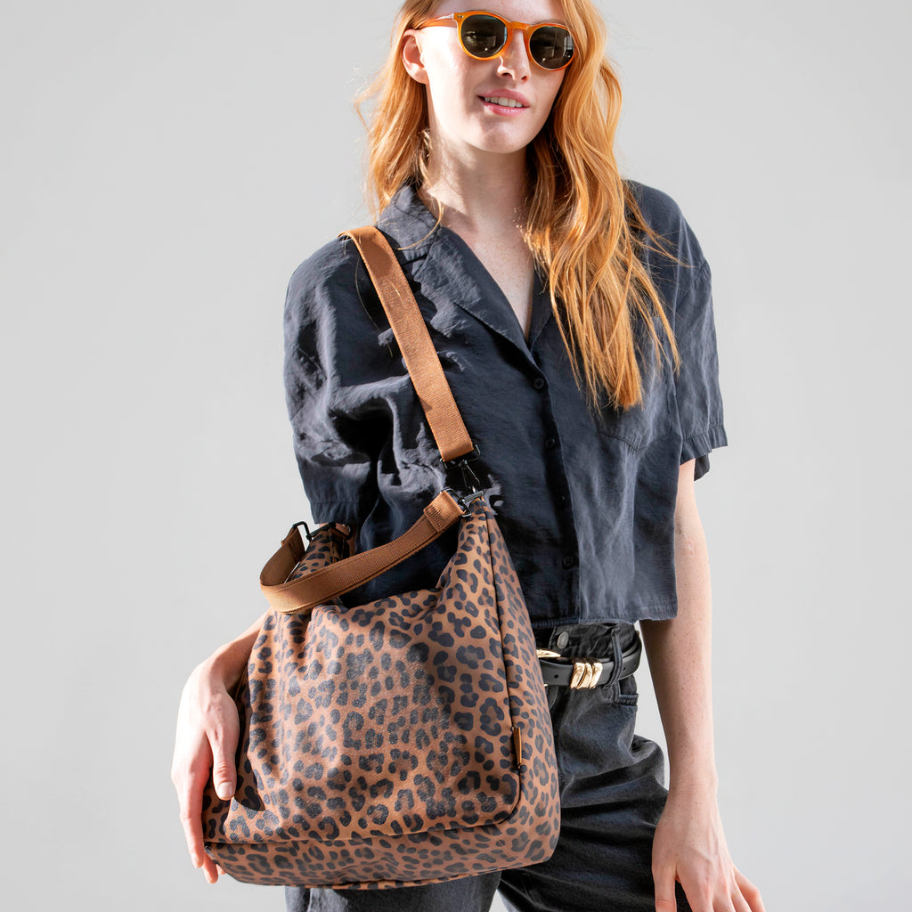 Woman wearing the large brown leopard Canvelle Hobo Handbag crossbody, front view, to show hands-free style.