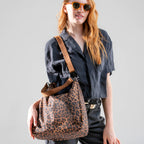 Woman wearing the large brown leopard Canvelle Hobo Handbag crossbody, front view, to show hands-free style.