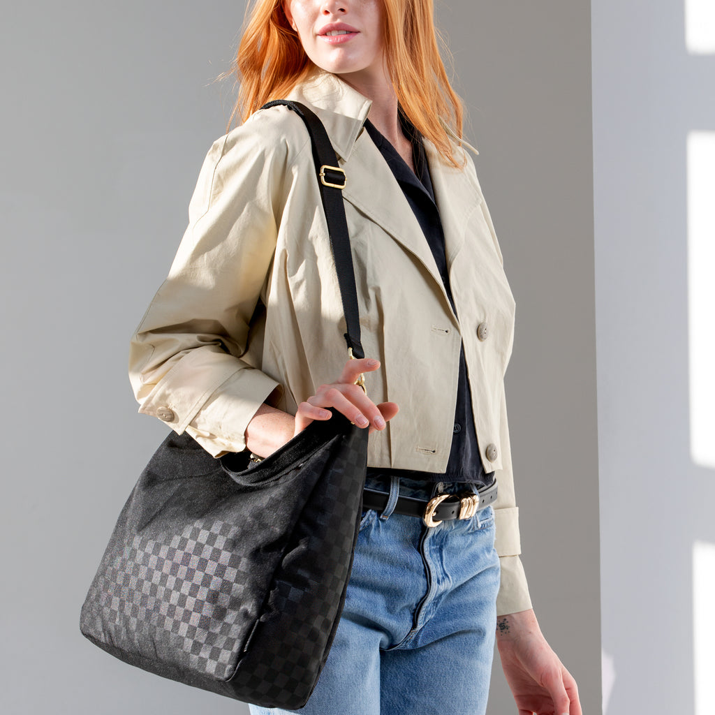 Woman wearing the large black checkered Canvelle Hobo Handbag crossbody with the long adjustable strap to show hands-free style.