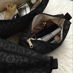 Three black leopard-print cosmetic pouches with gold zippers, shown open and filled with toiletries, arranged on a white faux-fur rug over a gray tiled floor.