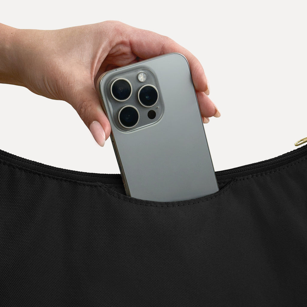 Phone sliding into the exterior back slip pocket of the large black Canvelle Hobo Handbag.