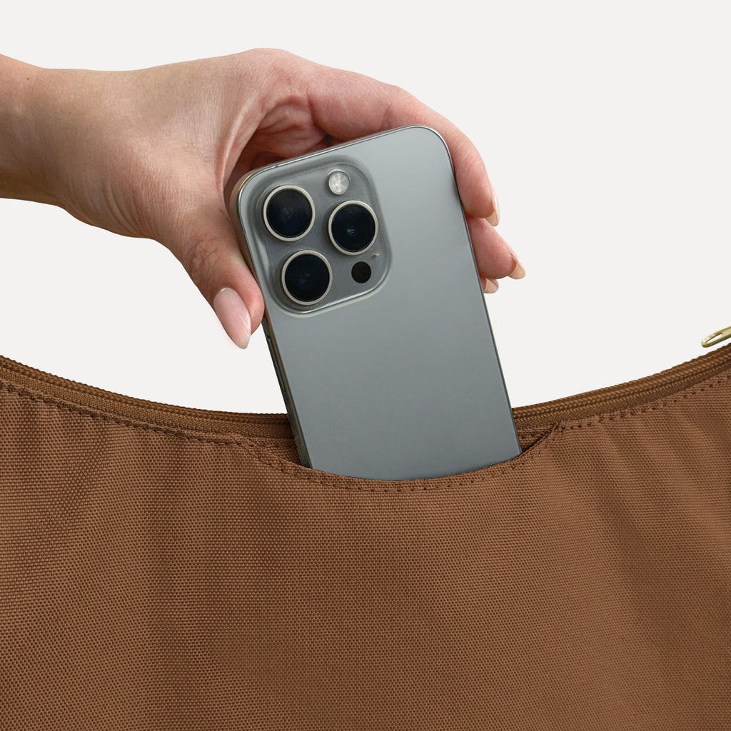 Phone sliding into the exterior back slip pocket of the large brown Canvelle Hobo Handbag.