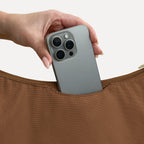 Phone sliding into the exterior back slip pocket of the large brown Canvelle Hobo Handbag.