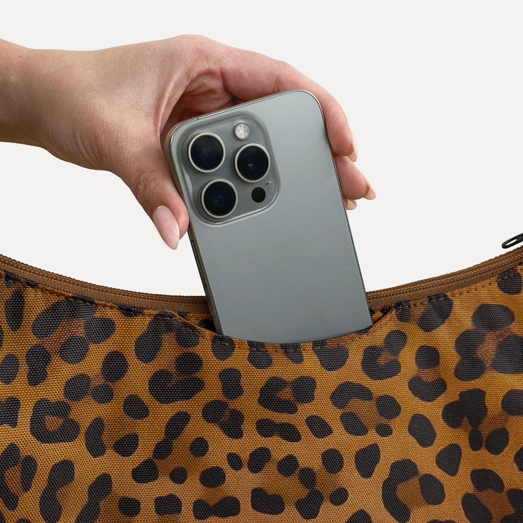 Phone sliding into the exterior back slip pocket of the large brown leopard Canvelle Hobo Handbag.