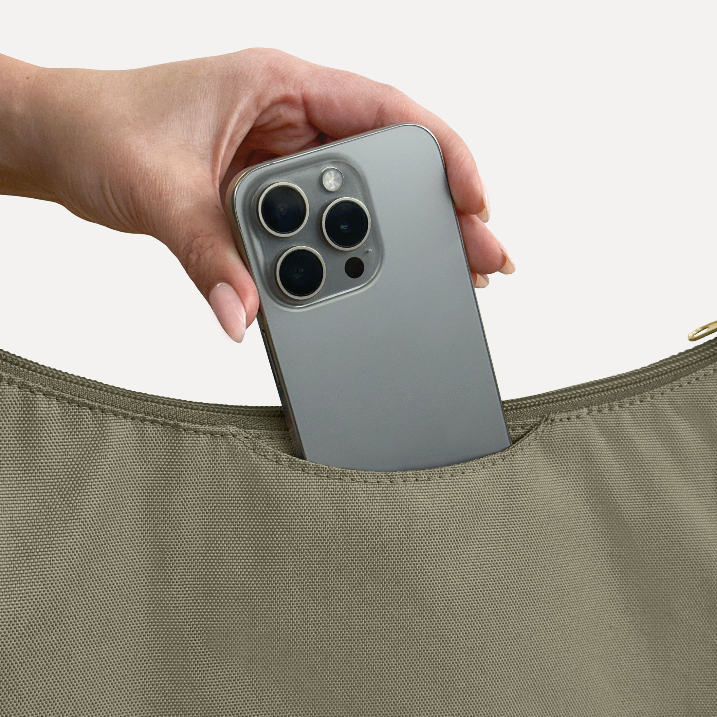 Phone sliding into the exterior back slip pocket of the large olive Canvelle Hobo Handbag.
