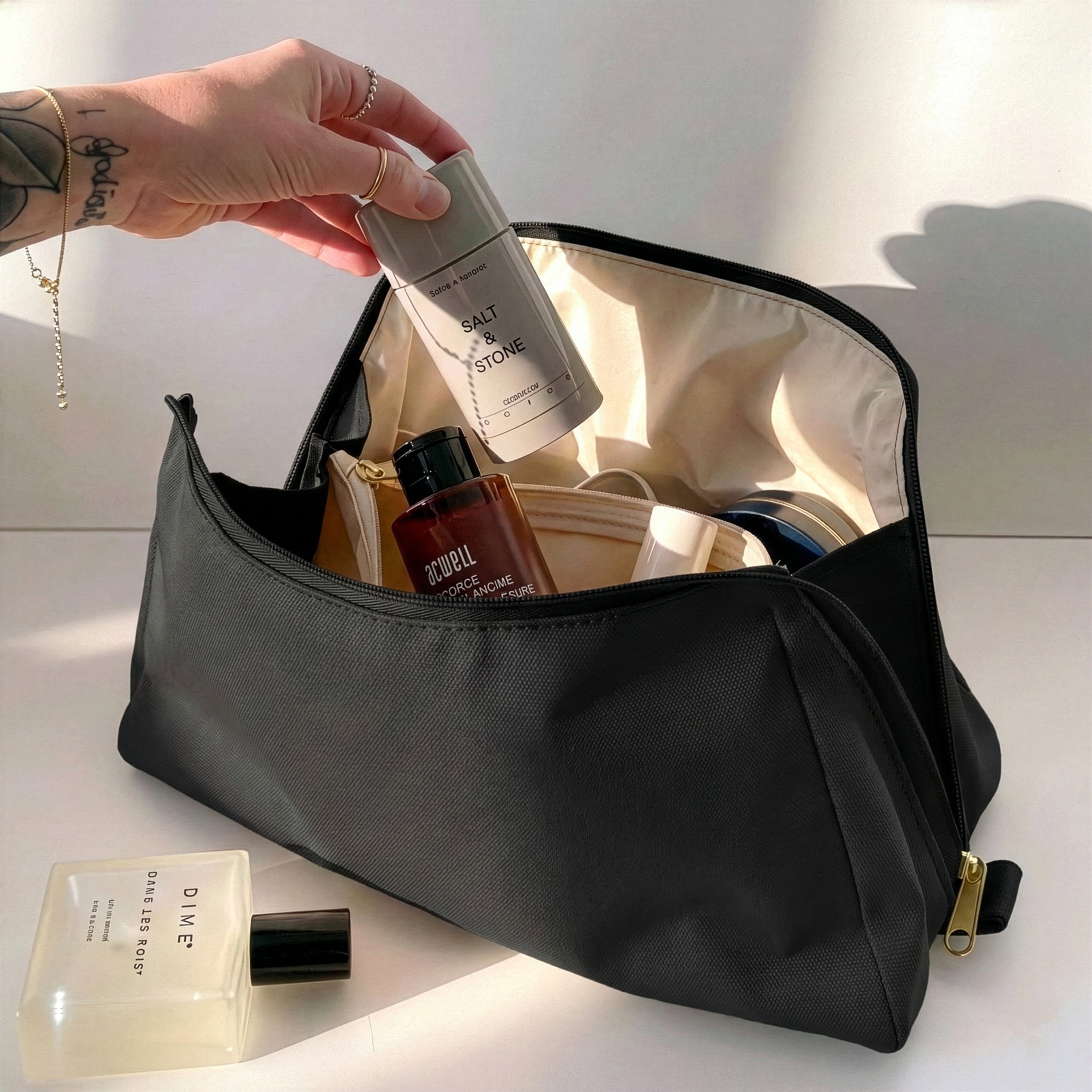 Woman packing large black Canvelle Toiletry Bag with travel essentials like Salt & Stone deodorant to demonstrate capacity and wide opening.