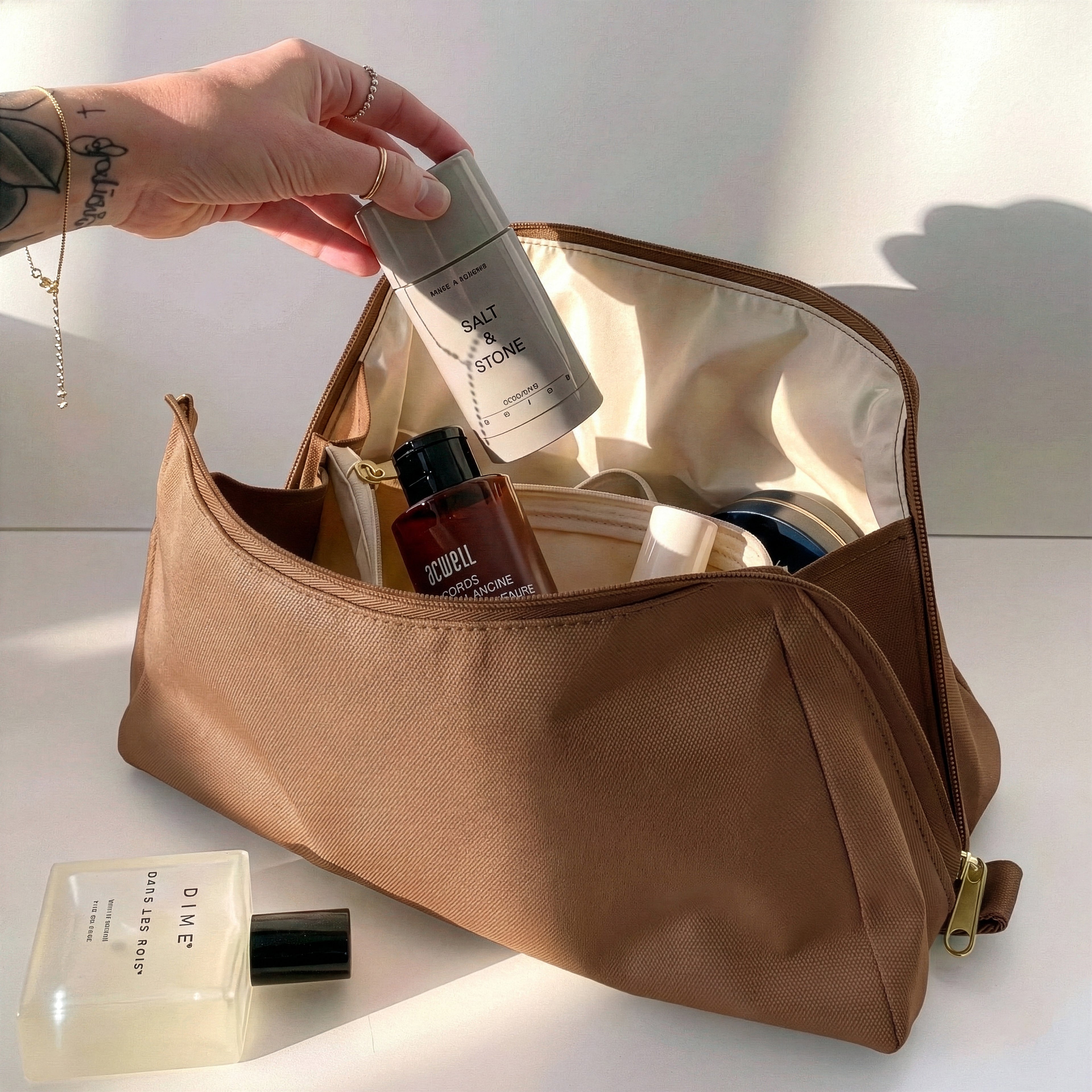 Woman packing large brown Canvelle Toiletry Bag with travel essentials like Salt & Stone deodorant to demonstrate capacity and wide opening.