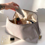 Open large grey Canvelle Toiletry Bag being packed with full-size skincare products including Salt & Stone deodorant and Dime perfume to demonstrate spacious capacity.