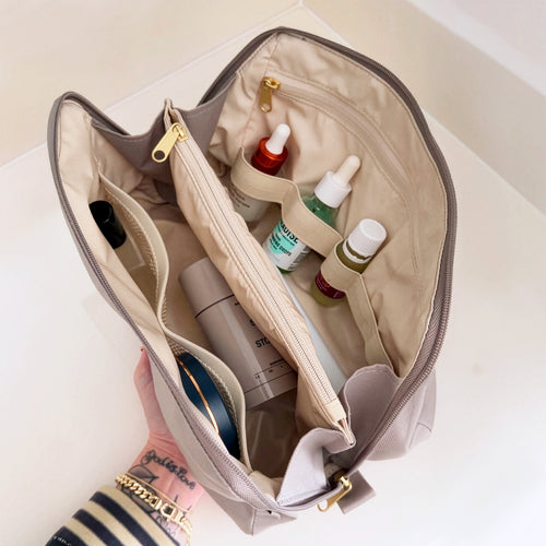 Top-down view of organized grey Canvelle Toiletry Bag holding skincare serums, Dime perfume, and toiletries in upright elastic loops and dividers.