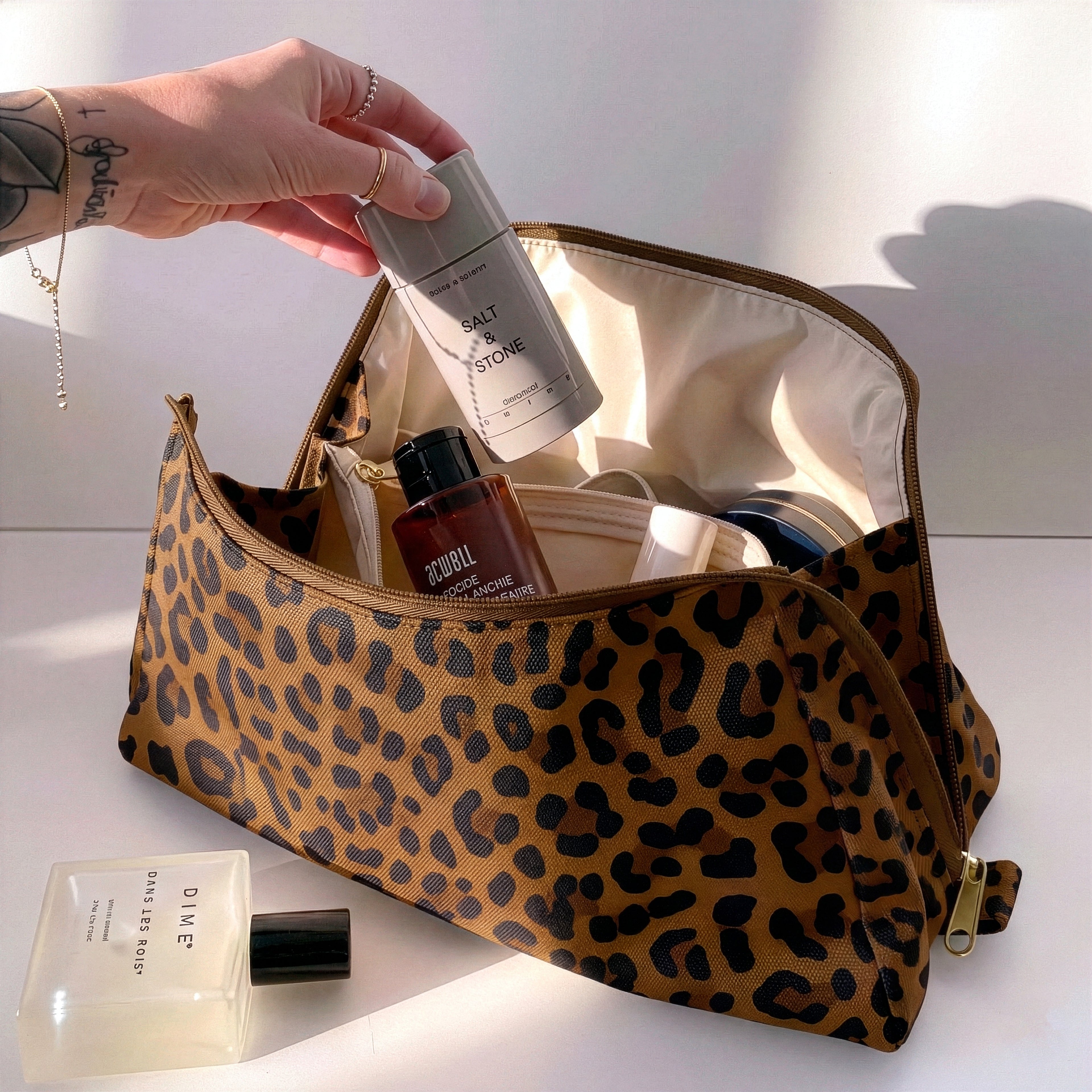 Woman packing large brown leopard print Canvelle Toiletry Bag with travel essentials like Salt & Stone deodorant to demonstrate capacity and wide opening.