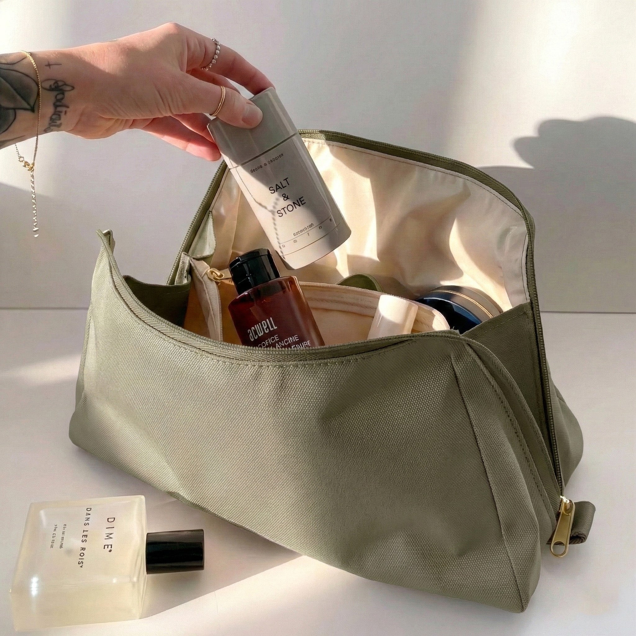Woman packing large olive green Canvelle Toiletry Bag with travel essentials like Salt & Stone deodorant to demonstrate capacity and wide opening.