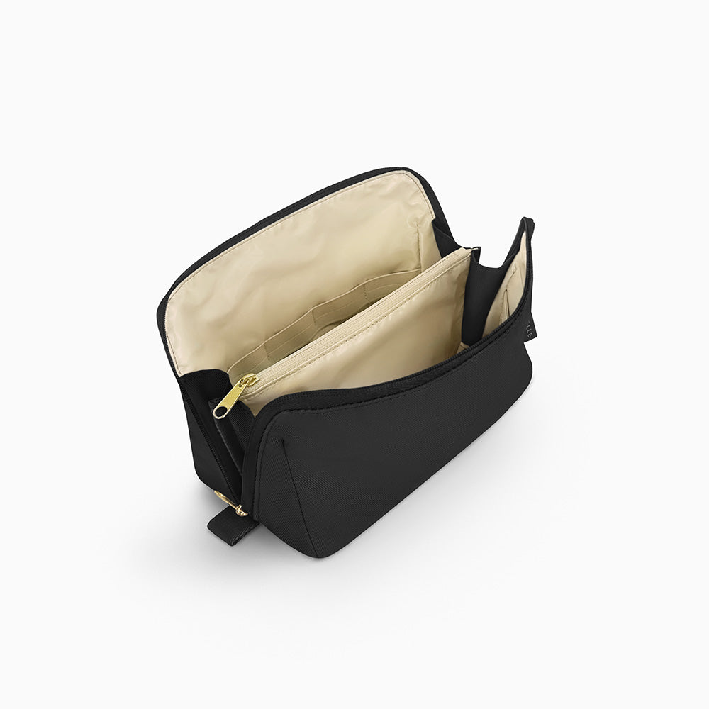 Open Canvelle Toiletry Bag in medium black showing beige water-resistant lining, central zipper divider pocket, and elastic loops for organization.