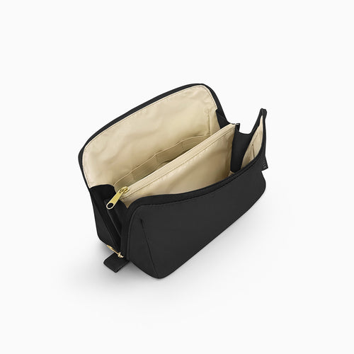 Open Canvelle Toiletry Bag in medium black showing beige water-resistant lining, central zipper divider pocket, and elastic loops for organization.