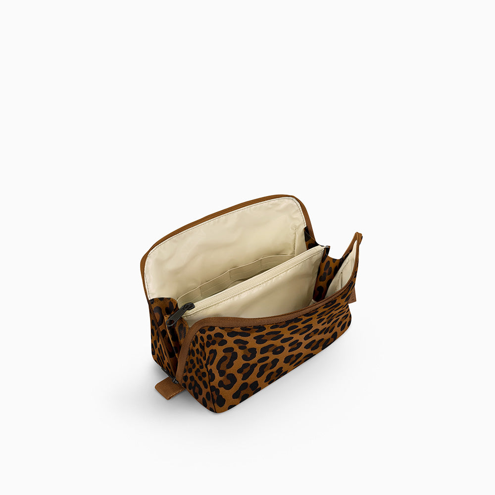 Open Canvelle Toiletry Bag in medium brown leopard print showing beige water-resistant lining, central zipper divider pocket, and elastic loops for organization.